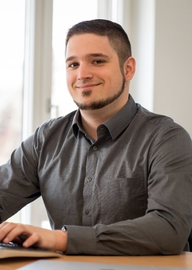 Benjamin, ein Mann, sitzt mit einem Laptop an einem Schreibtisch.