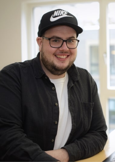 Reto Stadelmann, ein Mann mit Brille und Nike-Mütze, sitzt an einem Schreibtisch.