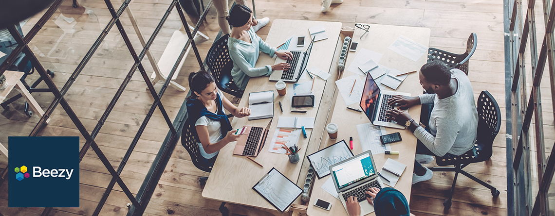 Eine Gruppe von Menschen, die mit Laptops an einem Tisch arbeiten und mit Beezy einen effizienten digitalen Arbeitsplatz schaffen.